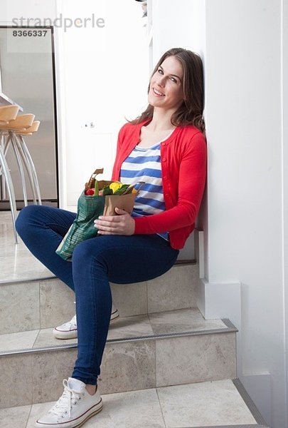 Junge Frau sitzend auf Küchenstufe mit Einkaufstasche