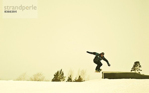 Junge männliche Snowboarder in der Luft am Berg