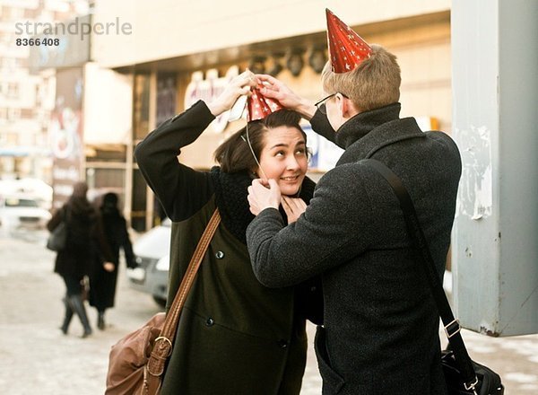 Junges Paar auf der Stadtstraße  das Partyhüte anpasst.