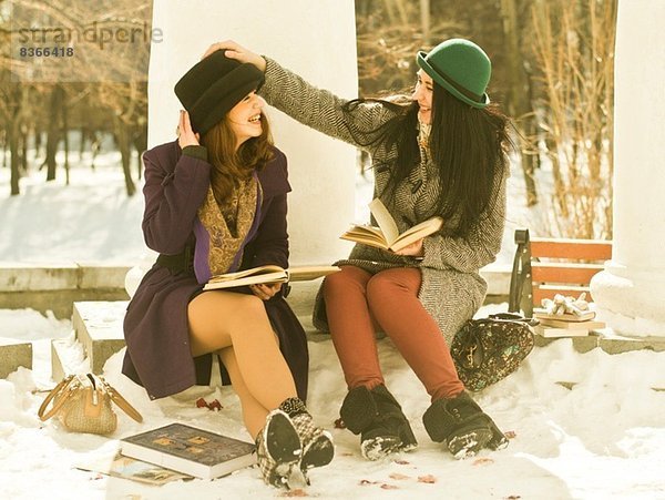 Zwei junge Frauen mit Büchern auf der Parkbank im Schnee