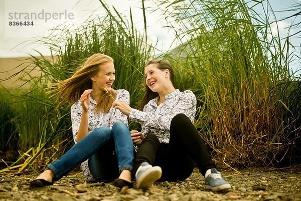 Zwei junge Frauen  die im Wind lachen.
