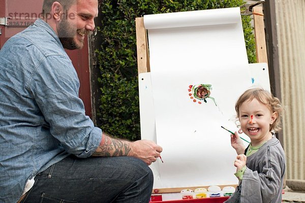 Vater albert herum und macht Farbe auf das Gesicht der Tochter.