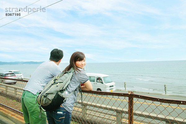 Junges Paar lehnt am Zaun und schaut aufs Meer