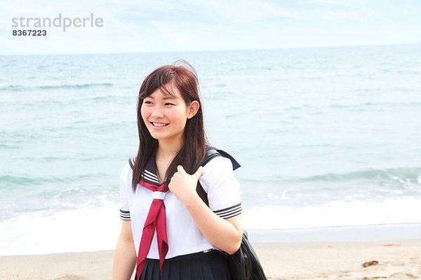 Junge Frau in Schuluniform am Strand stehend