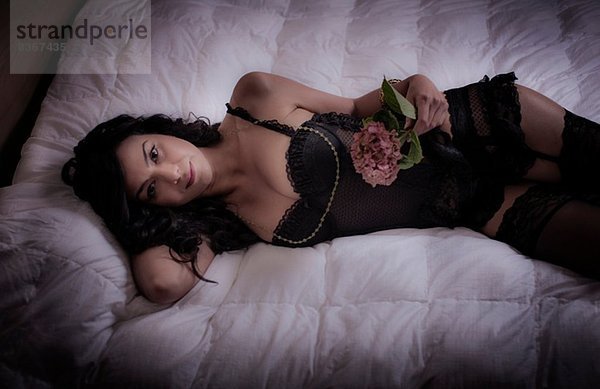 Mittlere erwachsene Frau  die auf dem Bett liegt und eine Blume hält.