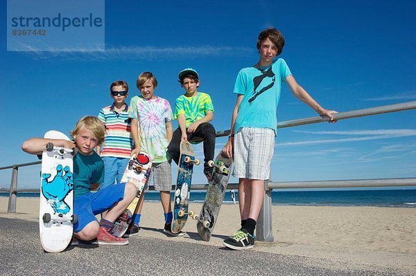 Portrait von fünf Jungen mit Skateboards an der Küste