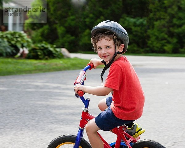 Porträt eines kleinen Jungen  der mit dem Fahrrad auf der Einfahrt fährt