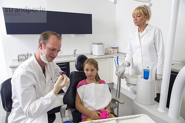 Zahnarzt bespricht die weitere Behandlung mit einem Mädchen und zeigt ihr eine Zahnspange  Deutschland