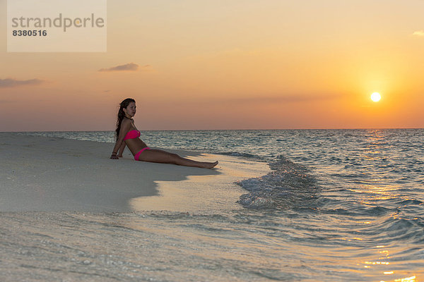 Frau sitzt am Strand bei Sonnenuntergang  Indischer Ozean  Malediven