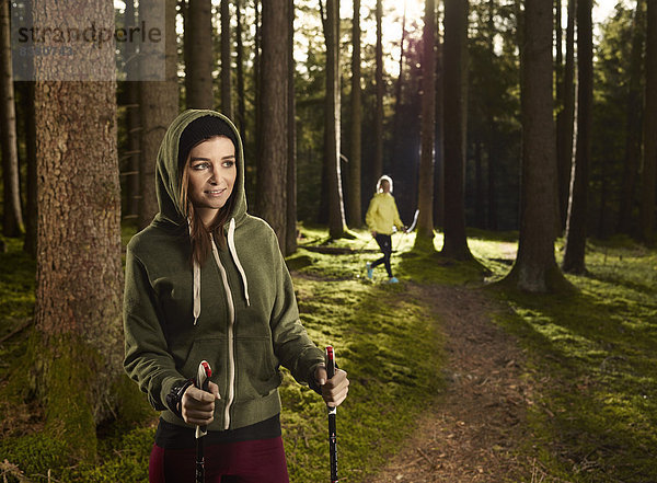 Frau mit Nordic-Walking-Stöcken im Wald  hinten joggt eine weitere Frau  Tirol  Austria