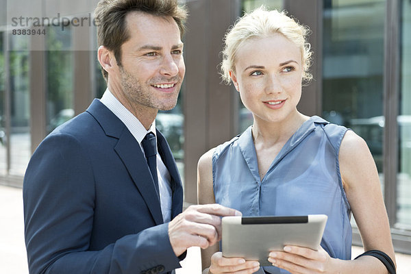 Immobilienmakler mit digitalem Tablett  das dem potentiellen Käufer die Immobilie zeigt.