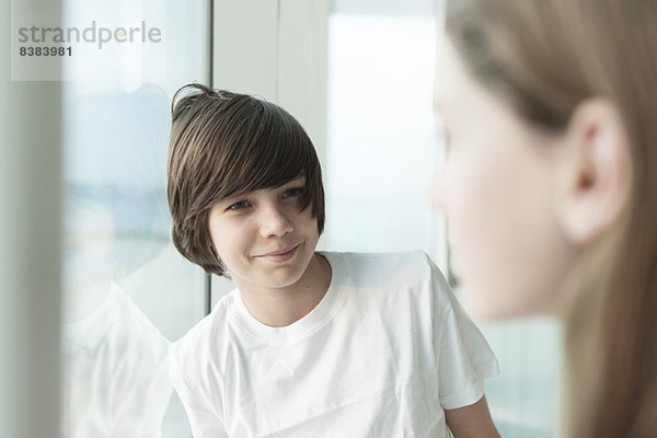 Teenager-Junge lehnt am Fenster und lächelt das Mädchen im Vordergrund an.