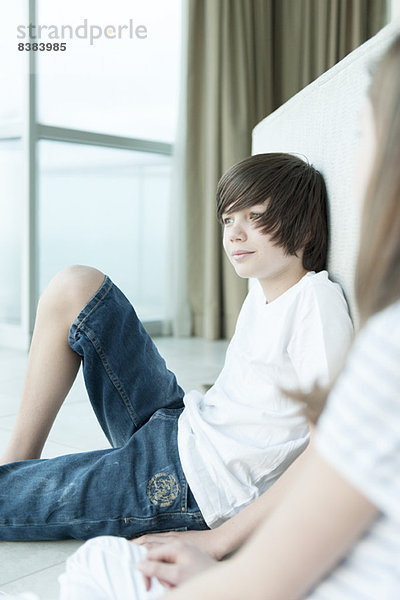 Teenager-Junge sitzt auf dem Boden und schaut aus dem Fenster.