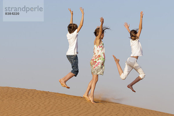 Kinder springen auf Sand  Rückansicht