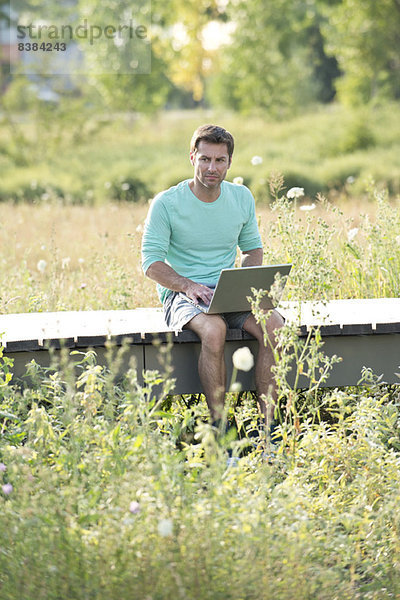 Mann  der einen Laptop benutzt  während er auf dem Land sitzt.