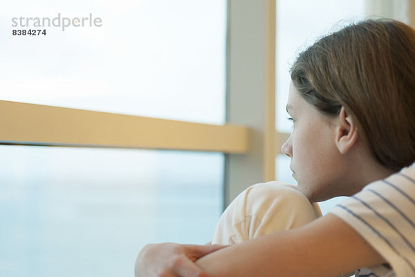 Preteen Mädchen Knie umarmend  aus dem Fenster schauend