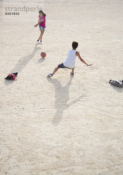 Kinder spielen mit Fußball im Sand