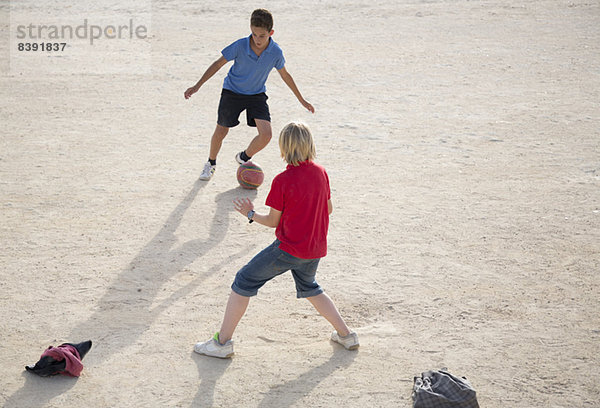 Jungen spielen mit Fußball im Sand