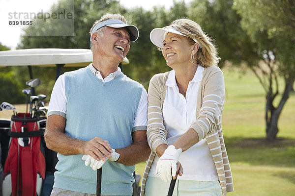 Seniorenpaar lacht auf dem Golfplatz