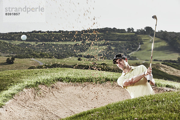 Mann schwingt aus Sandfang auf dem Golfplatz