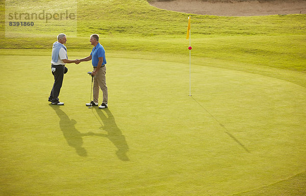 Ältere Männer beim Händeschütteln auf dem Golfplatz