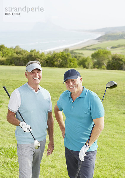 Senioren lächeln auf dem Golfplatz mit Blick auf den Ozean