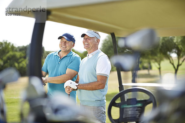 Ältere Männer stehen neben dem Golfwagen.