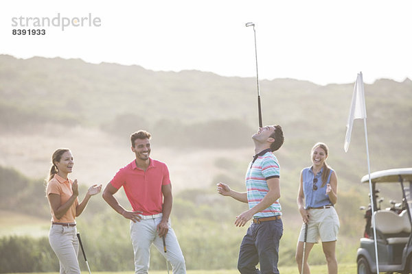 Freunde beobachten Mann Gleichgewicht Golfschläger auf der Nase