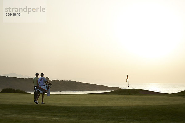 Männer auf dem Golfplatz bei Sonnenuntergang