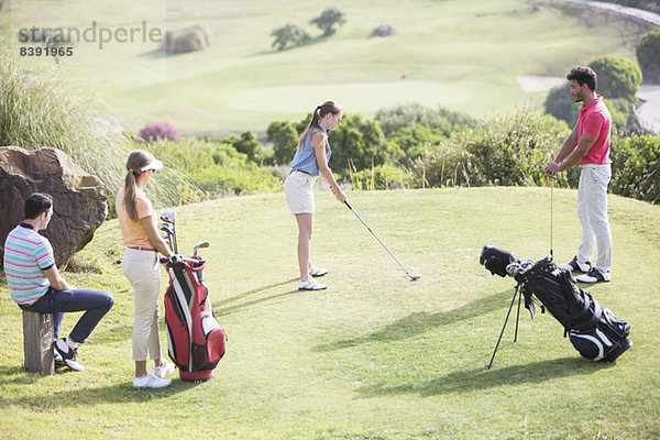 Freunde beobachten Frau beim Abschlag auf dem Golfplatz