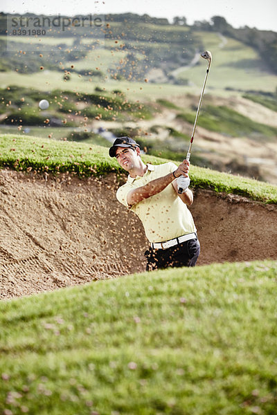 Mann schwingt aus Sandfang auf dem Golfplatz