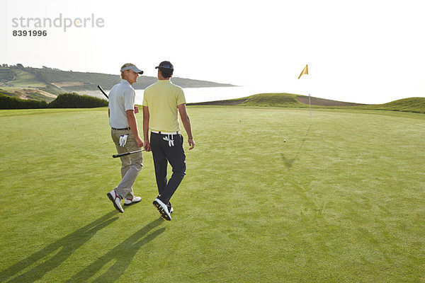 Männer  die zum Loch auf dem Golfplatz mit Blick auf den Ozean gehen.