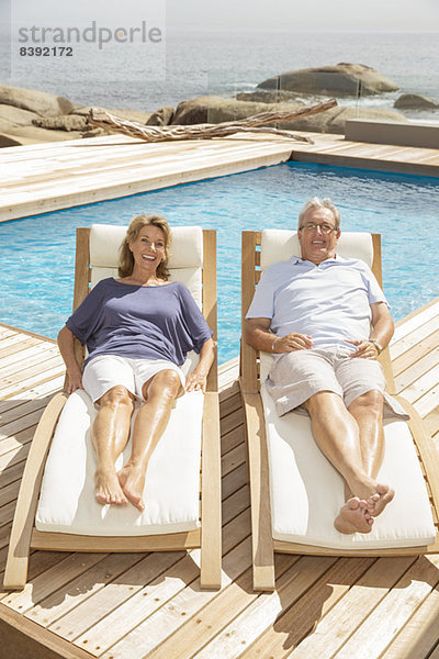 Seniorenpaar auf Liegestühlen am Pool liegend