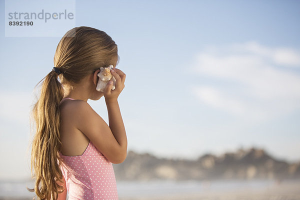 Mädchen hört Muschel am Strand