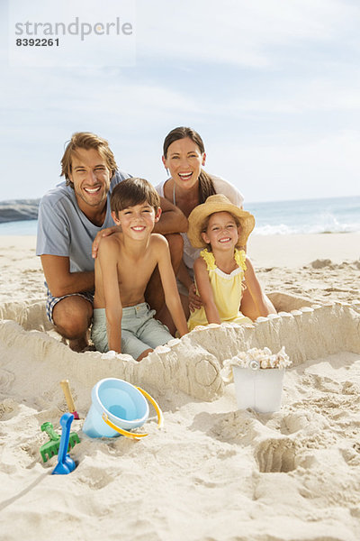 Familie sitzt in einer Sandburg am Strand