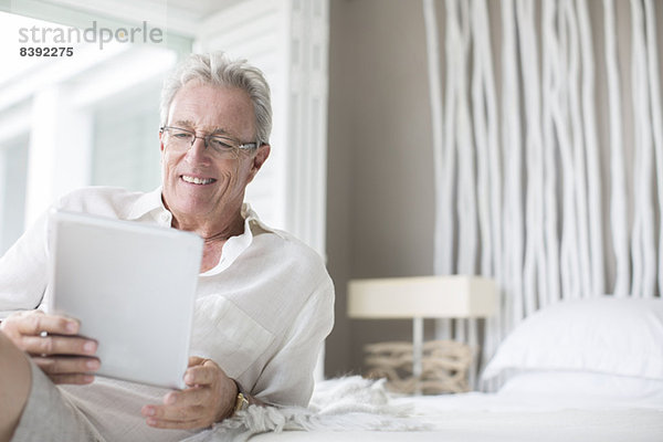 Älterer Mann mit digitalem Tablett auf dem Bett