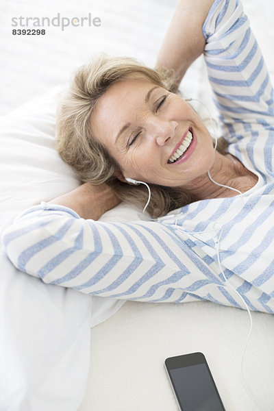 Ältere Frau hört Kopfhörer auf dem Bett