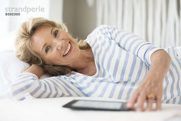 Ältere Frau mit digitalem Tablett auf dem Bett