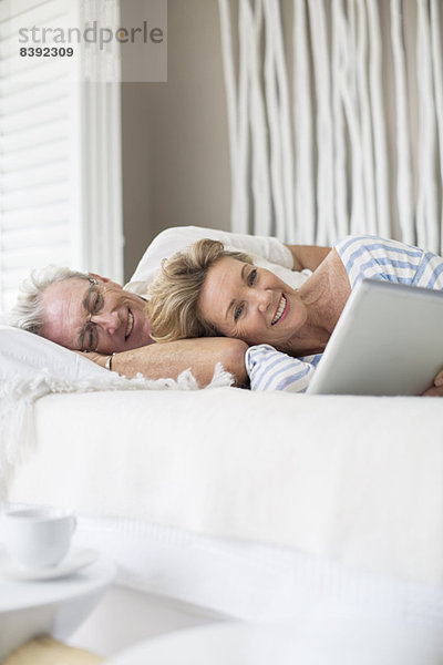 Älteres Paar mit digitalem Tablett auf dem Bett