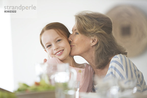 Ältere Frau küsst Enkelin bei Tisch