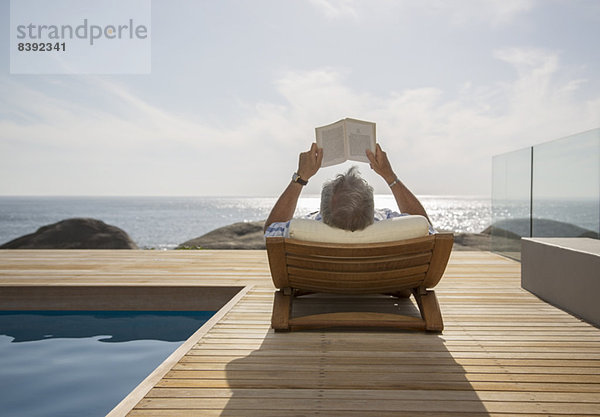 Älterer Mann beim Lesen am Pool