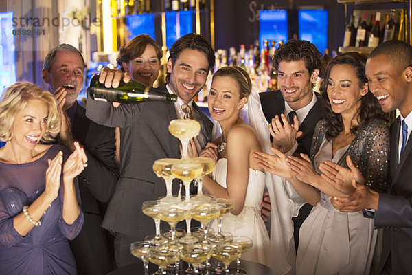 Braut und Gruppe gießen Champagnerpyramide bei der Hochzeitsfeier