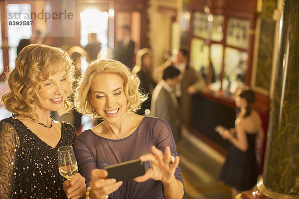 Gut gekleidete Frauen beim Blick auf das Handy in der Theaterlobby