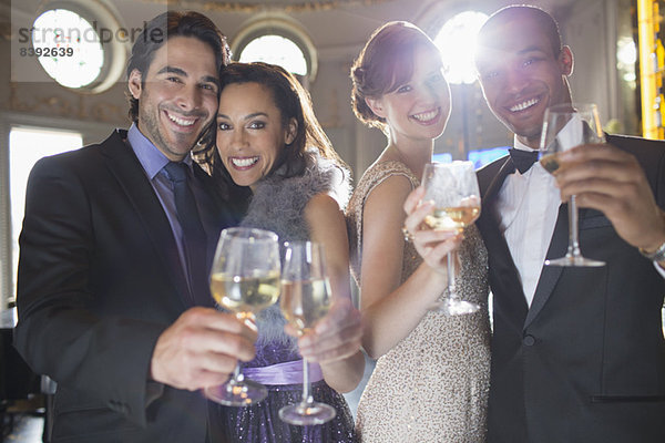 Porträt von gut gekleideten Paaren  die auf Champagner und Weingläser anstoßen.