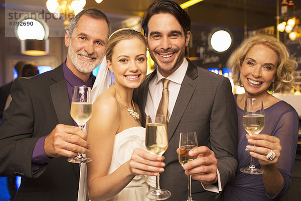 Porträt der glücklichen Braut und des Bräutigams beim Toasten von Champagnerflöten mit den Eltern