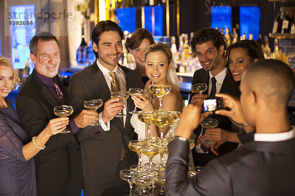 Mann fotografiert Braut und Bräutigam mit Freunden in der Champagnerpyramide
