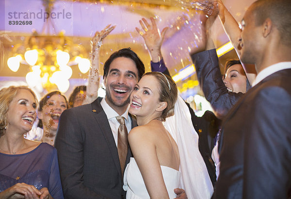 Freunde werfen Konfetti über Braut und Bräutigam bei der Hochzeitsfeier