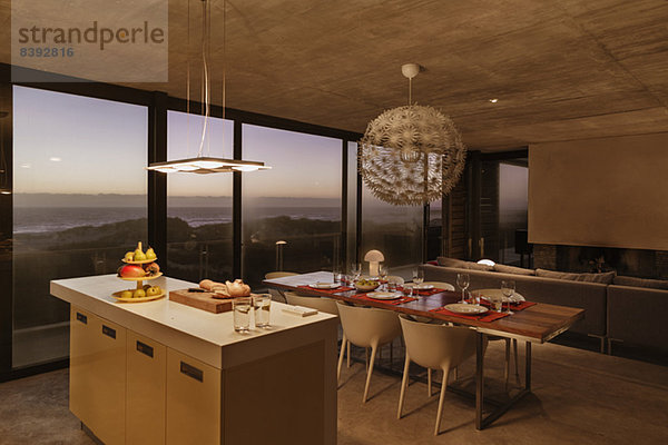 Frühstücksbar und Esstisch in moderner Küche mit Blick auf das Meer in der Abenddämmerung