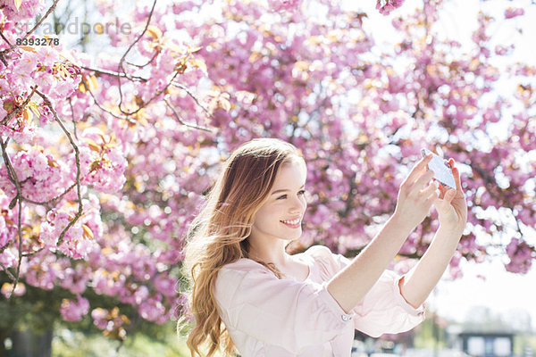 Frau beim Selbstbildnis unter Baum mit rosa Blüten