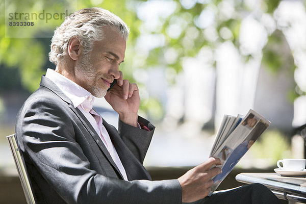 Geschäftsmann liest Magazin auf dem Bürgersteig Cafe